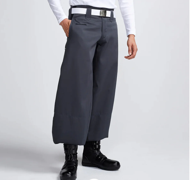 A man wearing dark gray wide-leg Japanese work pants with a white long-sleeve shirt, white belt, and black work boots, standing against a light gray background.