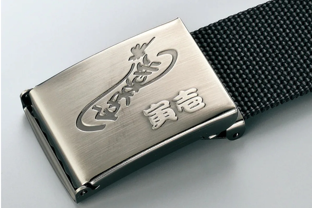 A close-up of a silver metal belt buckle engraved with Japanese characters, attached to a black woven work belt.