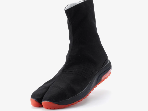 A black split-toe Japanese work boot with a black sole and bright orange tread, shown at an angle against a plain light gray background.