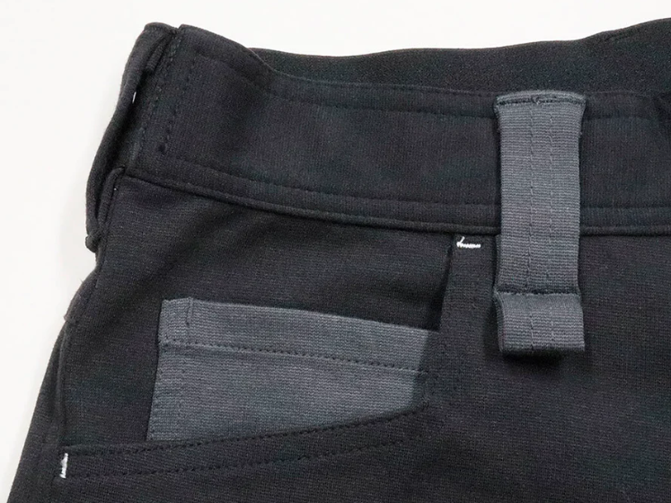 A close-up of black work pants featuring a reinforced pocket, belt loop, and contrast gray fabric detail.