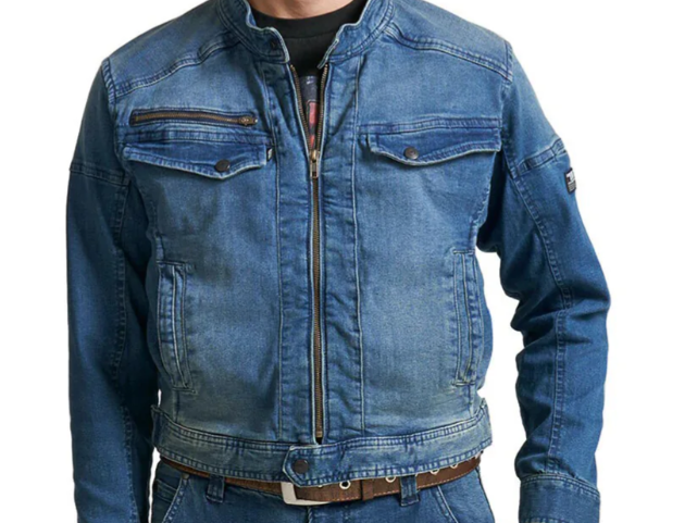 A model wearing a blue denim work jacket with a stand collar, front zipper, zippered chest pocket, and flap chest pockets, shown against a light gray background.