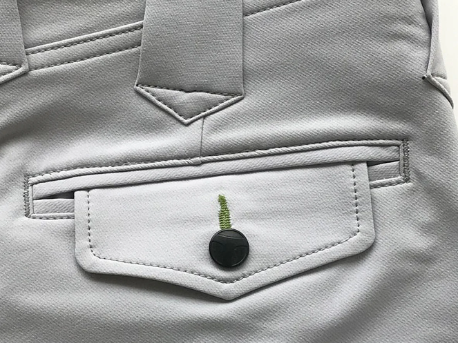 A close-up of light gray work pants featuring a flap pocket with a black button, belt loop, and stitched welt pocket detail.