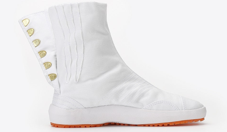 A white split-toe Japanese work boot with side fasteners, a white sole, and bright orange tread, shown from the side against a light gray background.