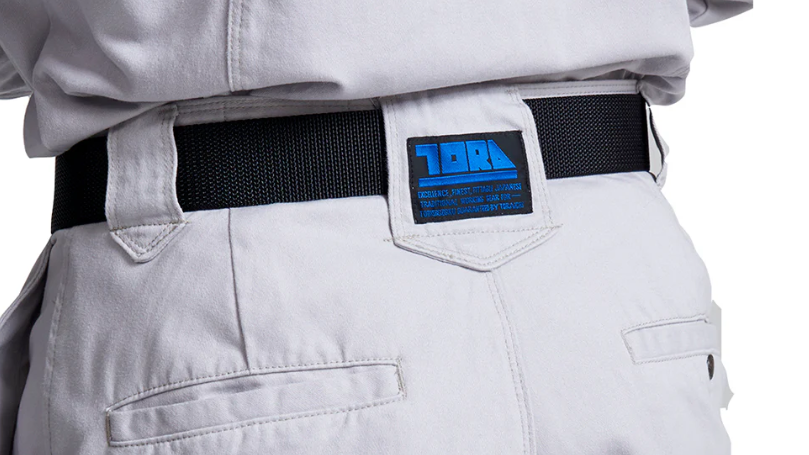 A close-up of the back waist of light gray work pants featuring a black belt, belt loops, back pockets, and a blue brand label.