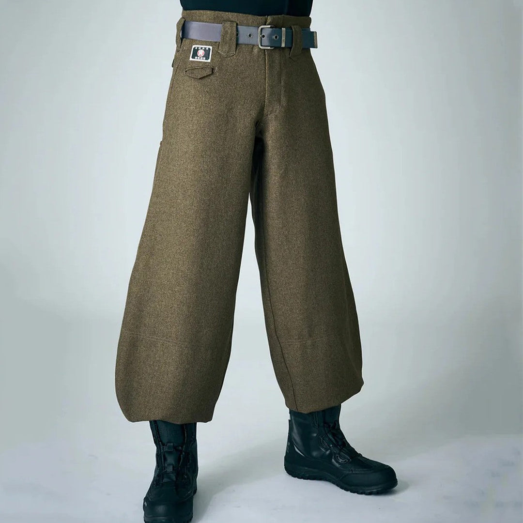 A model wearing brown wide-leg Japanese tobi work pants with a belt and black work boots, shown against a plain light gray background.