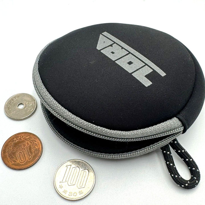 Toraichi coin case in black with grey trim, displayed with Japanese yen coins, representing durable tobi workwear accessory